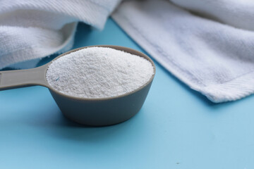 Detergent powder in measuring spoon with towel. Laundry concept.