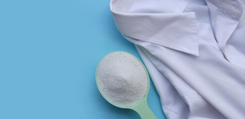 Detergent powder in measuring spoon on cloth before washing. Laundry concept.