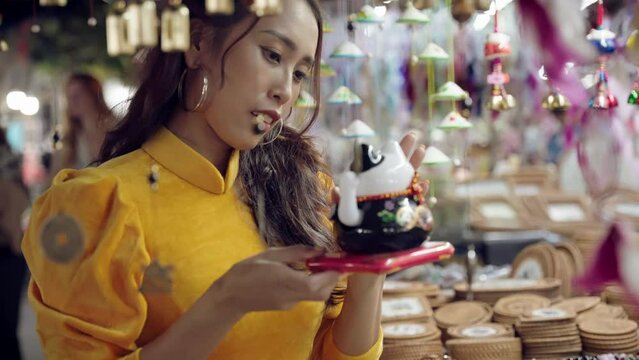 Woman in yellow Ao Dai admiring a lucky cat souvenir at Hoi An market, vibrant colors, evening