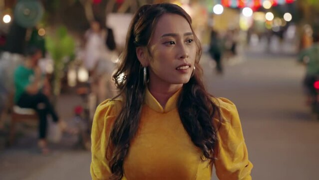 Close up slow motion shot of Vietnamese woman in yellow dress walking with thinking expression at night, Hoi An, Vietnam