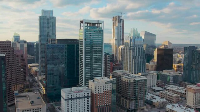 Drone flyover Austin Texas iconic downtown tower district overlooking Frost Bank Tower, The Austonian, JW Marriot Hotel, and the Westin in a beautiful golden sunset with clouds.