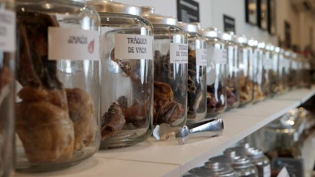 Rows of old fashioned glass jars filled with dried dog treats displayed with serving tongs in pet shop