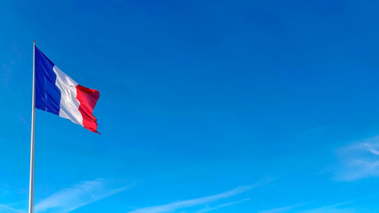 The French flag is fluttering in the wind against the clear blue sky. Copy space for text