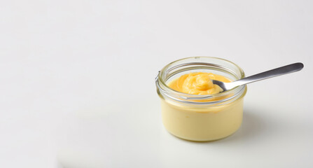 A small mason jar on a white background holds orange butter, a spoon beside it, underlined by dark yellow and silver intense lines.