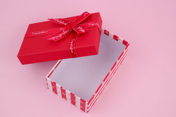 Open red gift box with words congratulations on ribbon on pink background.	