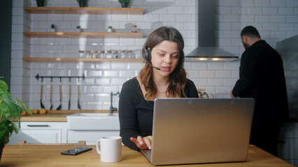 Focused representative call center agent in wireless headset helping client with complaints using laptop. Female operator working at home in kitchen, customer support service on helpline telesales	
