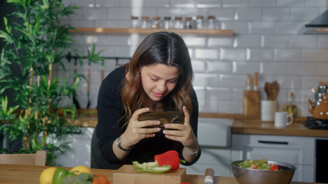 Girl taking picture or recording video with smartphone the vegetables and fruits on kitchen table. Blogger woman preparing food, taking pictures on phone for her social accounts or video stories	