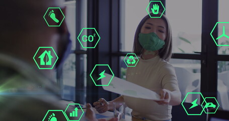 Image of ecology icons over asian businesswoman with face mask holding document