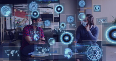 Image of digital screens over diverse business people wearing face masks and using laptop