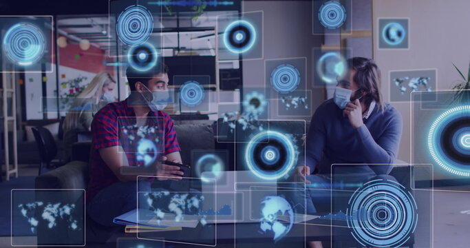 Image of digital screens over diverse business people wearing face masks and using laptop