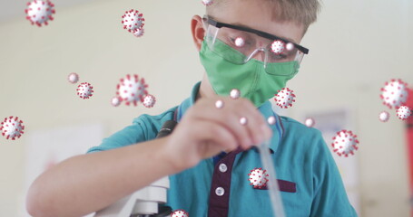 Multiple covid-19 cells floating against boy wearing face mask performing experiment in laboratory