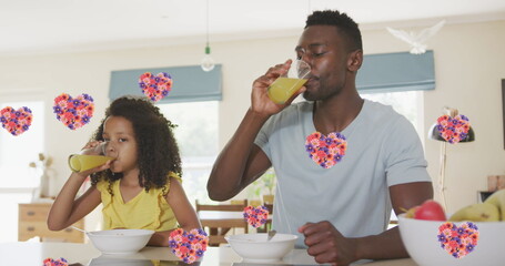Image of flower hearts over african american father and daughter drinking juice at home