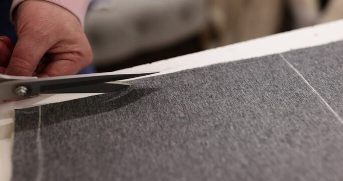 Hands of seamstress use scissors to cut markings on clothing