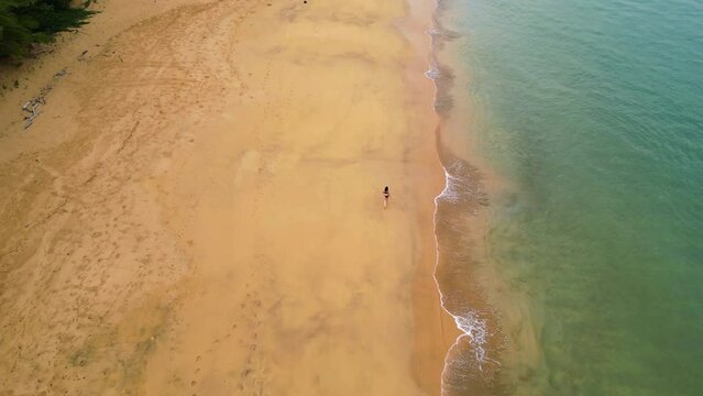 Aerial view following a woman walking on a empty beach in cloudy west Africa
