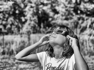 A young girl looking at the sun during a solar eclipse on a country park, family outdoor activity - 756977858