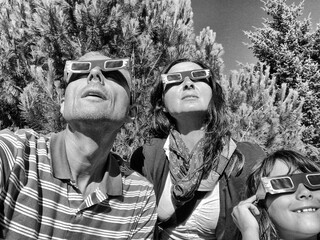 Father, mother and daughter, family viewing solar eclipse with special glasses in a park - 756977898