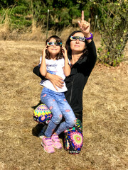 Mother and daughter, family viewing solar eclipse with special glasses in a park - 756979814