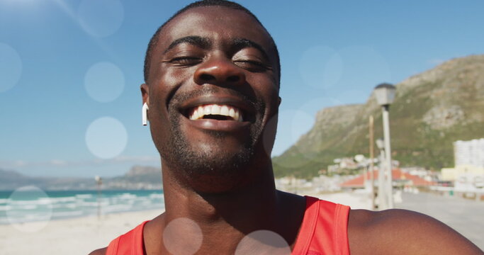 Image of glowing lights over happy exercising african american man making image call and waving