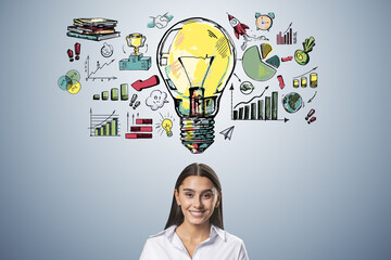 Portrait of happy young businesswoman with creative business sketch with huge light bulb and other...
