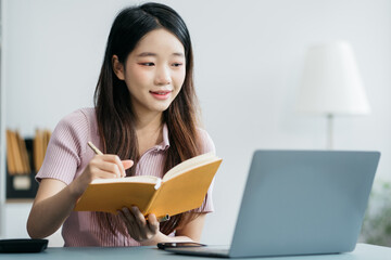 Female  use a Laptopand take notes in the notebook at the office desk in the morning.