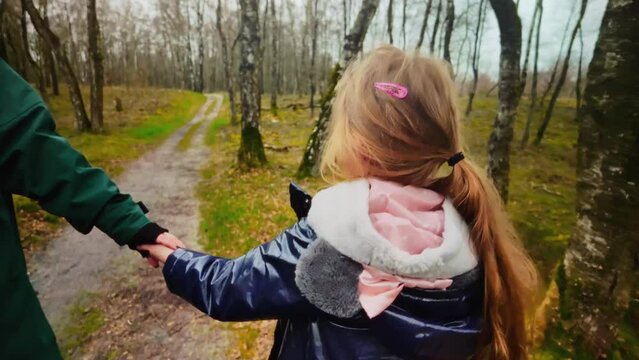 Daughter walks, holding her mother hand, through a nature reserve, filmed from behind