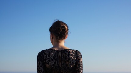 Woman with bun in her hair is looking out at ocean - obrazy, fototapety, plakaty