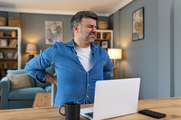 Shot of a businessman suffering from a backache while working at his desk in his office. Man having...