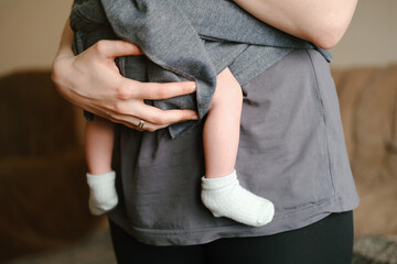 Mother with ergo baby carrying toddler at home in sling. While baby is sleeping. Tiny little feet in socks. 