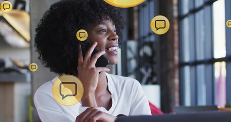 Multiple message icons floating against african american woman talking on smartphone at office