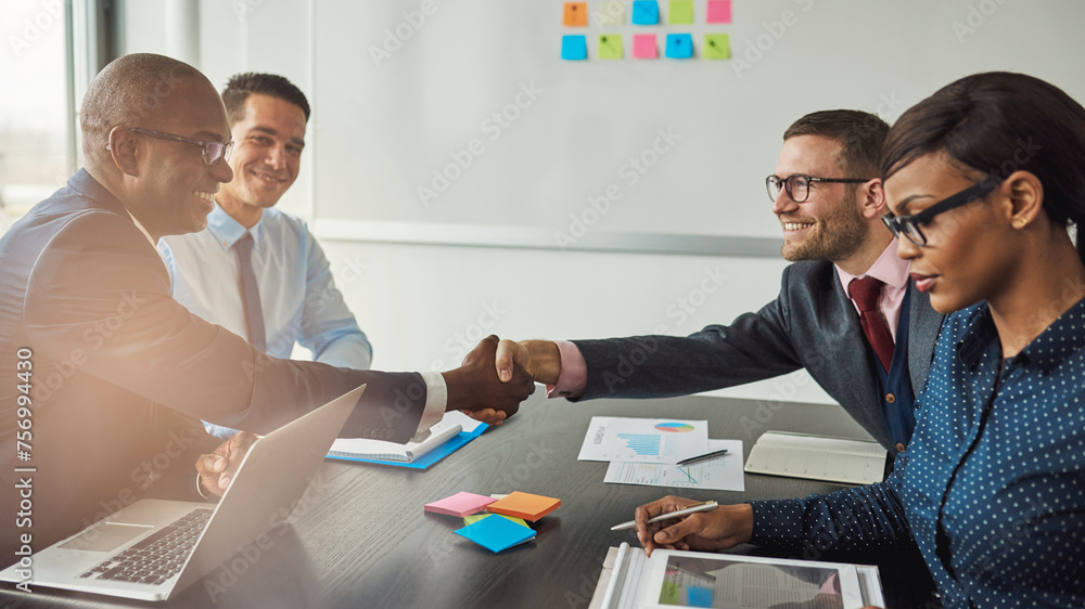 Wall mural Four multiracial business people are sitting at a negotiation table. They smile and shake hands on a successful deal they just made