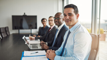 Multiracial executive business team working together in a modern workplace. Successful business team smiling cheerfully while sitting in a row at a boardroom table and looking direct into the camera - 756994488