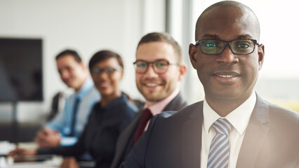 Group of multicultural businesspeople working together in a modern workplace. Successful business team smiling cheerfully while sitting in a row at a boardroom table and looking direct into the camera