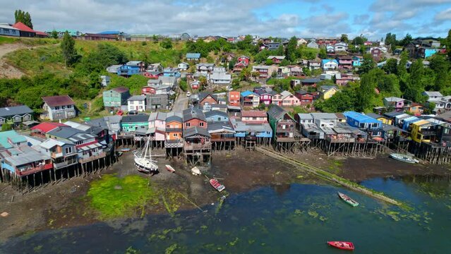 Aerial Drone Stilt house colorful village at island Sea Chilo&eacute; chilean Patagonia travel destination establishing shot, green islet hills with blue pacific ocean