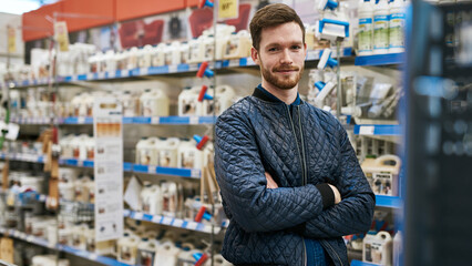 Confident smiling handyman with beard standing in a hardware store with arms crossed - 756996008