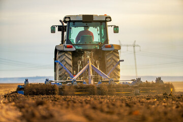 Tractor cultivating with dust and sunset backdrop