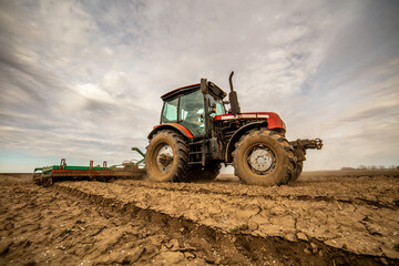 Agricultural scene of a tractor plowing dry soil, kicking up dust with a dramatic sky overhead
