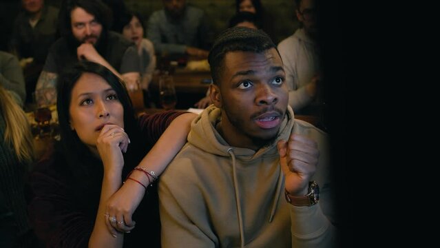 Group of diverse friends together watch live football match broadcast in sports pub on TV. Fans gathered to cheer and support team playing in tournament. Player scores a goal and crowd celebrate.