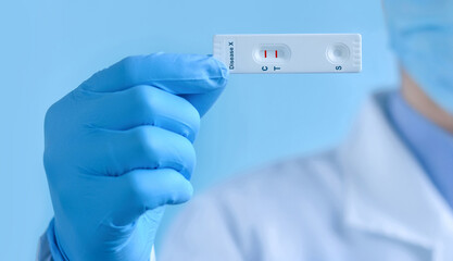 A doctor wearing a protective mask and gloves shows a rapid laboratory test for Disease X test ....