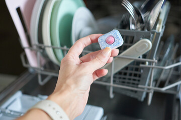 Close-up of woman's hand holding pill in dishwasher machine