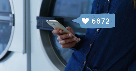 Close up of a man leaning on a washing machine while texting on his phone