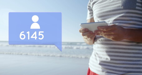 Close up of a Caucasian man standing on the beach while typing on his phone