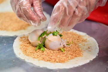 Fototapeta premium A vendor at the Ningxia Night Market in Taipei City, Taiwan, sprinkles cilantro on a peanut roll ice cream. The peanut roll ice cream is made with a crepe, two scoops of ice cream, and peanut brittle.