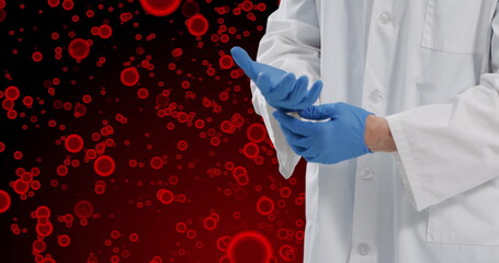 Image of midsection of caucasian male doctor with glove over red cells on red background