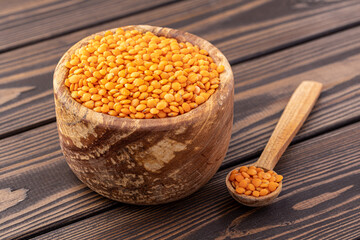 Photo of red lentils in wooden bowl with wooden measuring cup on wooden background.  Healthy lifestyle. Vegetarian and vegan diet.