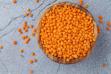 Photo of red lentils in wooden bowl with wooden measuring cup on wooden background.  Healthy lifestyle. Vegetarian and vegan diet.