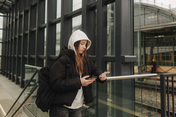Tourist teenage girl at train station using smartphone map, social media check-in, or buy ticket booking. Modern travel app technology, lone traveler, Winter vacation railroad adventure concept - 757022033
