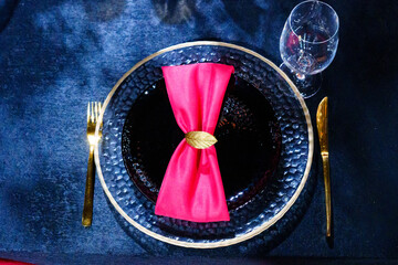 A black plate with a red napkin with a gold ring.  - Powered by Adobe