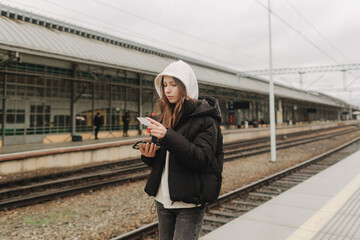 Tourist teenage girl at train station using smartphone map, social media check-in, or buy ticket booking. Modern travel app technology, lone traveler, Winter vacation railroad adventure concept - 757022487