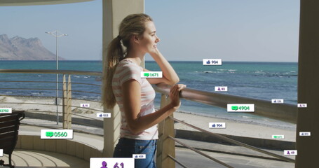 Image of social media icons on banners over relaxed caucasian woman admiring view by seaside