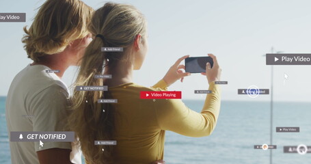 Multiple digital icons over rear view of caucasian couple taking picture of the sea from smartphone